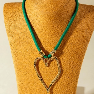 Detail of a large gold hammered heart pendant on a thick green braided cord necklace