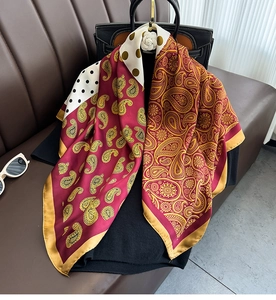 Detail of paisley and polka dot silk scarf draped on a leather handbag with soft texture