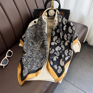 Elegant paisley print silk scarf with yellow border draped on beige knit sweater