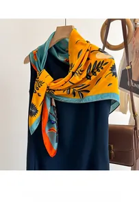 Detail of vibrant yellow satin scarf with teal leaf patterns tied on a navy top