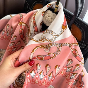 Pink and white silk scarf with equestrian chain print draped elegantly over a luxury handbag