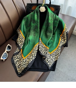Detail of satin floral silk scarf with leopard print edge draped over a black leather bag