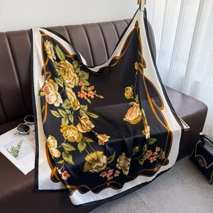Floral print satin square scarf with yellow roses draped over a luxury leather sofa