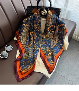 Detail of silk-like paisley square scarf with vibrant orange patterns on navy blue base