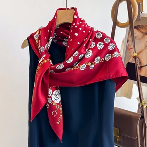 Detail of red silk scarf with white floral patterns and gold chain print on a hanger