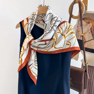 Elegant silk-like floral scarf with orange flower print styled on a wooden hanger