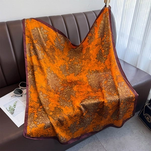 Carré de soie synthétique 90cm avec motifs floraux orange sur un canapé en cuir chic