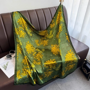 Détail d'un foulard en soie vert foncé avec imprimés floraux jaunes sur un canapé en cuir