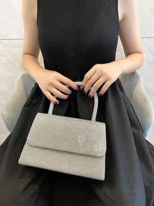Close-up of sparkling silver evening clutch bag held by model in black dress