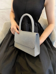 Sparkling silver glitter evening bag with curved handle held by model in black formal dress