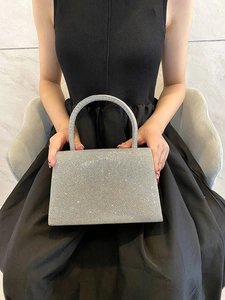 Detail of silver sparkling evening bag with round handle held by model in black dress