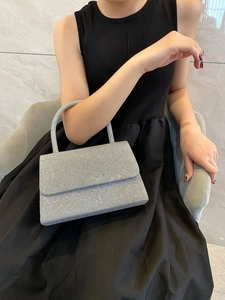 Silver sequin evening clutch bag held by model wearing a black dress in an elegant setting