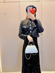 Detail of a white trapezoidal handbag with rhinestone buckle and metal handle on sequin outfit