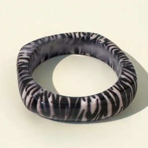 Detail of zebra pattern thick resin bangle in square geometric shape on beige background