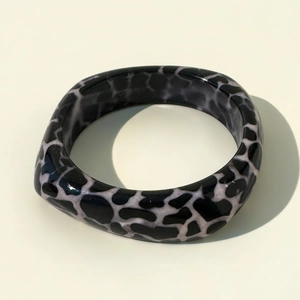 Close-up of wide resin bangle featuring black and white leopard print and glossy finish
