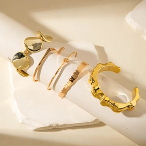 Detail of 5-piece gold geometric knot bracelets and textured bangles set on white stand