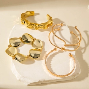 Detail of four gold geometric cuff bracelets on white marble tray with soft shadows