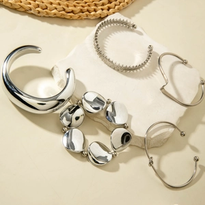Macro detail of glossy silver geometric knotted cuff and wavy metallic bracelet set