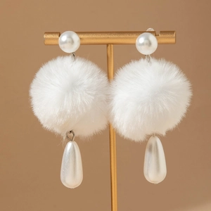 Detail of white fluffy pom pom earrings with pearls on a golden jewelry stand