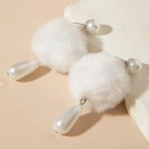 Detailed macro of plush white fur balls and water-drop pearl pendant earrings on marble