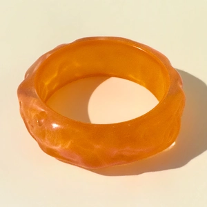 Macro shot of orange resin bracelet showing irregular wavy texture and translucent finish