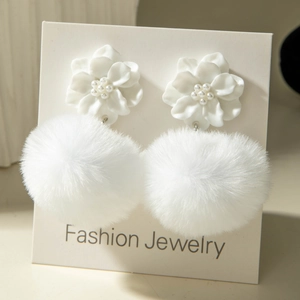 Close-up of white resin flower and fluffy faux fur pom-pom earrings with pearl centers