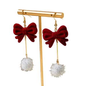 Red velvet bow and white pompom drop earrings on a golden display stand