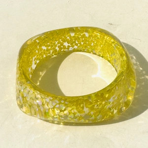 Close-up of translucent yellow resin bangle with silver glitter and thick square frame