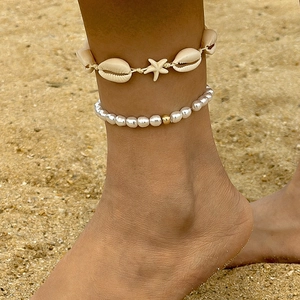 Detalle de un set de tobilleras playeras con conchas naturales y estrella de mar en arena
