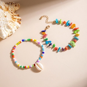 Detalle de set de tobilleras de cuentas de colores con colgante de concha blanca de playa