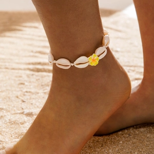 Detalle de tobillera playera con conchas blancas y flor de plumeria sobre la arena