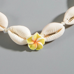 Detalle macro de conchas naturales y flor de plumeria amarilla en tobillera tejida