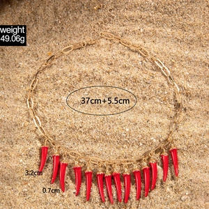 Gros plan du collier chaîne dorée avec piments rouges et dimensions sur fond de sable