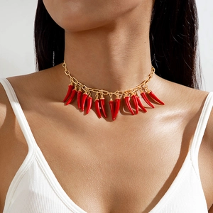 Gros plan d'un choker doré avec pendentifs piments rouges vifs sur un débardeur blanc
