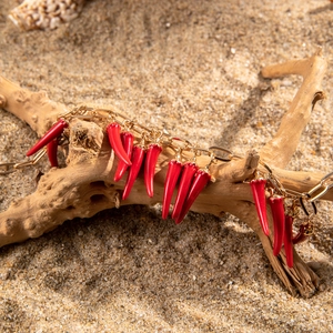 Détail d'un collier chaîne dorée avec pendentifs piment corail rouge sur sable