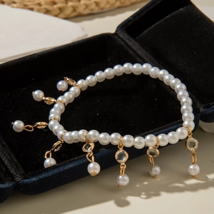 Detalle de tobillera de perlas blancas con colgantes dorados sobre terciopelo azul