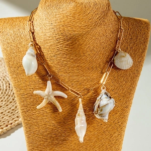 Détail d'un collier trombone doré avec des pendentifs corail et coquillages sur support