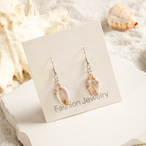 Detailed view of natural shell earrings displayed on sand with starfish beach elements
