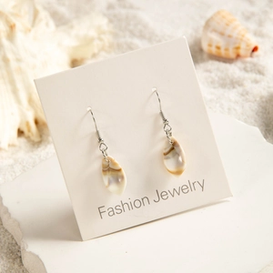 Detailed view of beach-style shell leaf earrings on a fashion display card with sand background
