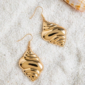 Detailed close-up of golden conch shell earrings on white sand beach background