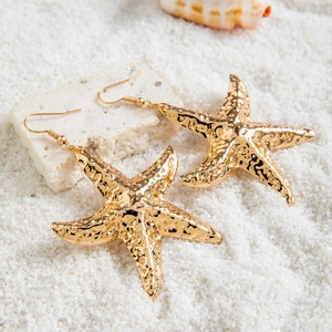 Detail of gold starfish earrings with hammer texture on white sand and seashells