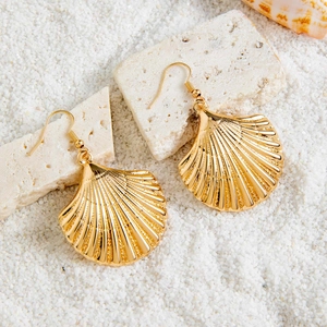 Detailed view of gold scallop shell earrings on white sand with ocean shells