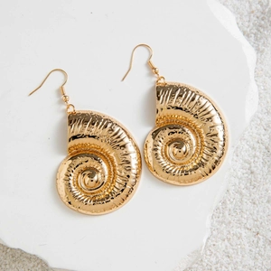 Detail of golden spiral shell earrings with textured finish on a beach sand background
