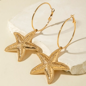 Detail of gold starfish hoop earrings with textured finish on a neutral stone background