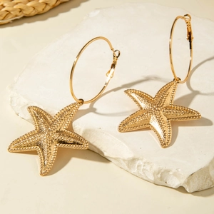 Close-up of golden starfish earrings with textured surface on a summer beach backdrop