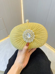 Macro detail of gold pleated satin clutch featuring a luxury rhinestone floral centerpiece