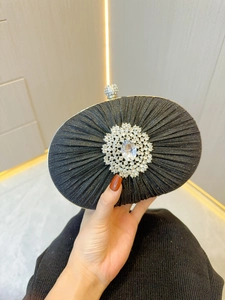 Close-up of elegant black pleated evening clutch with sparkling rhinestone brooch
