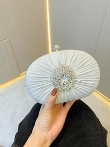 Close-up of silver pleated satin evening clutch featuring a radial rhinestone buckle