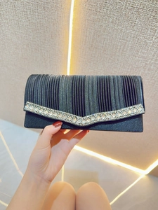 Close-up of black evening clutch bag with elegant pleated fabric and V-shaped crystal trim
