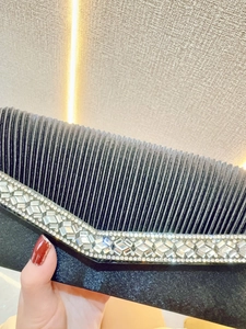 Detail of black pleated evening clutch featuring V-shaped rhinestone embellishments